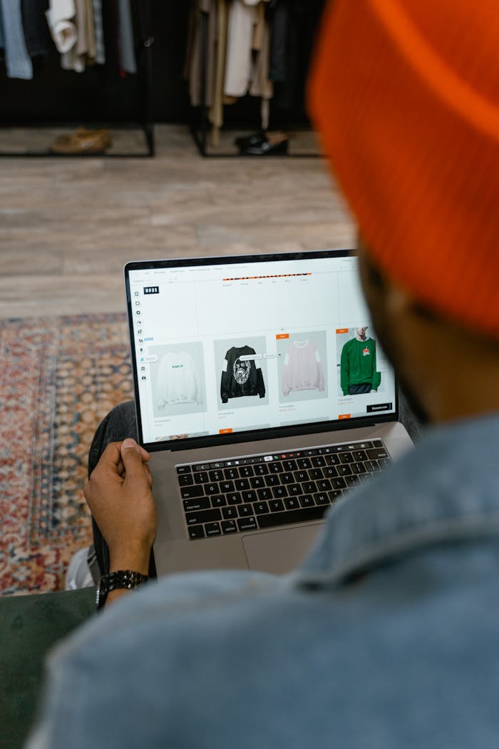 Adult man browsing clothing options on a laptop in a cozy indoor setting.